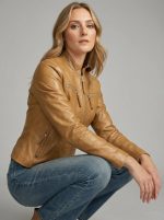 Women's tan leather cafe racer jacket styled casually in a seated lifestyle pose